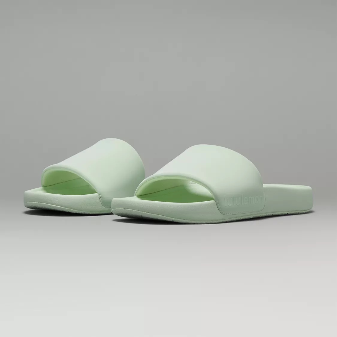 A pair of pale green slide sandals with a single wide strap over the foot.