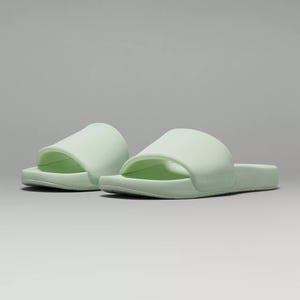 A pair of pale green slide sandals with a single wide strap over the foot.