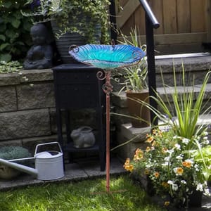 The Canora Grey Glass Bird Bath features a blue glass bowl with decorative swirls on a tall, slender metal stand, designed for garden use.