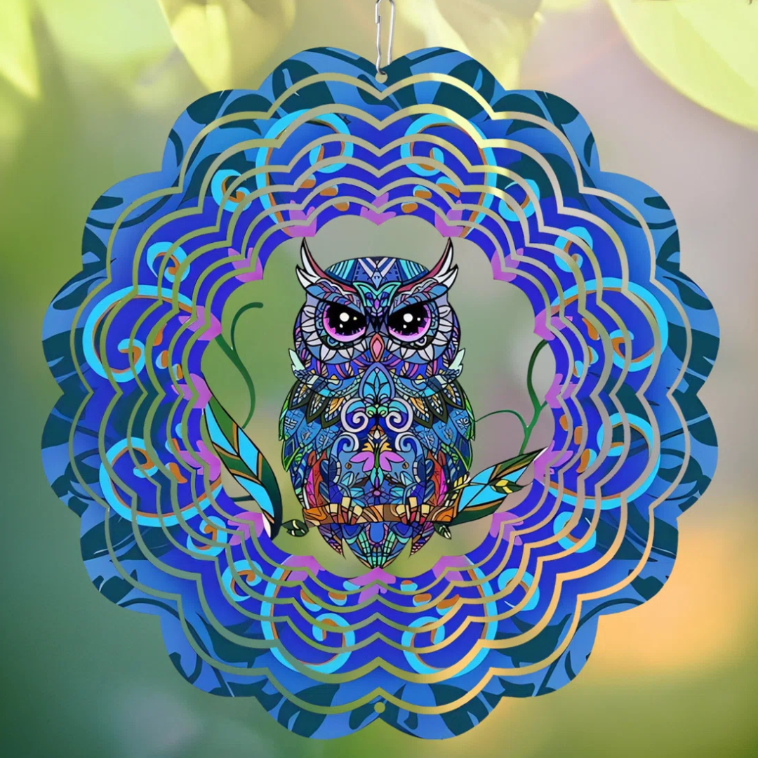 A colorful, mandala-style owl wind spinner featuring intricate patterns and vibrant blues, purples, and greens, hangs against a blurred natural background.