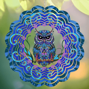 A colorful, mandala-style owl wind spinner featuring intricate patterns and vibrant blues, purples, and greens, hangs against a blurred natural background.