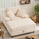 A cream-colored, ribbed fabric sofa with two pillows, featuring an extended chaise. It is placed in a living room setting with wooden and modern decor elements.