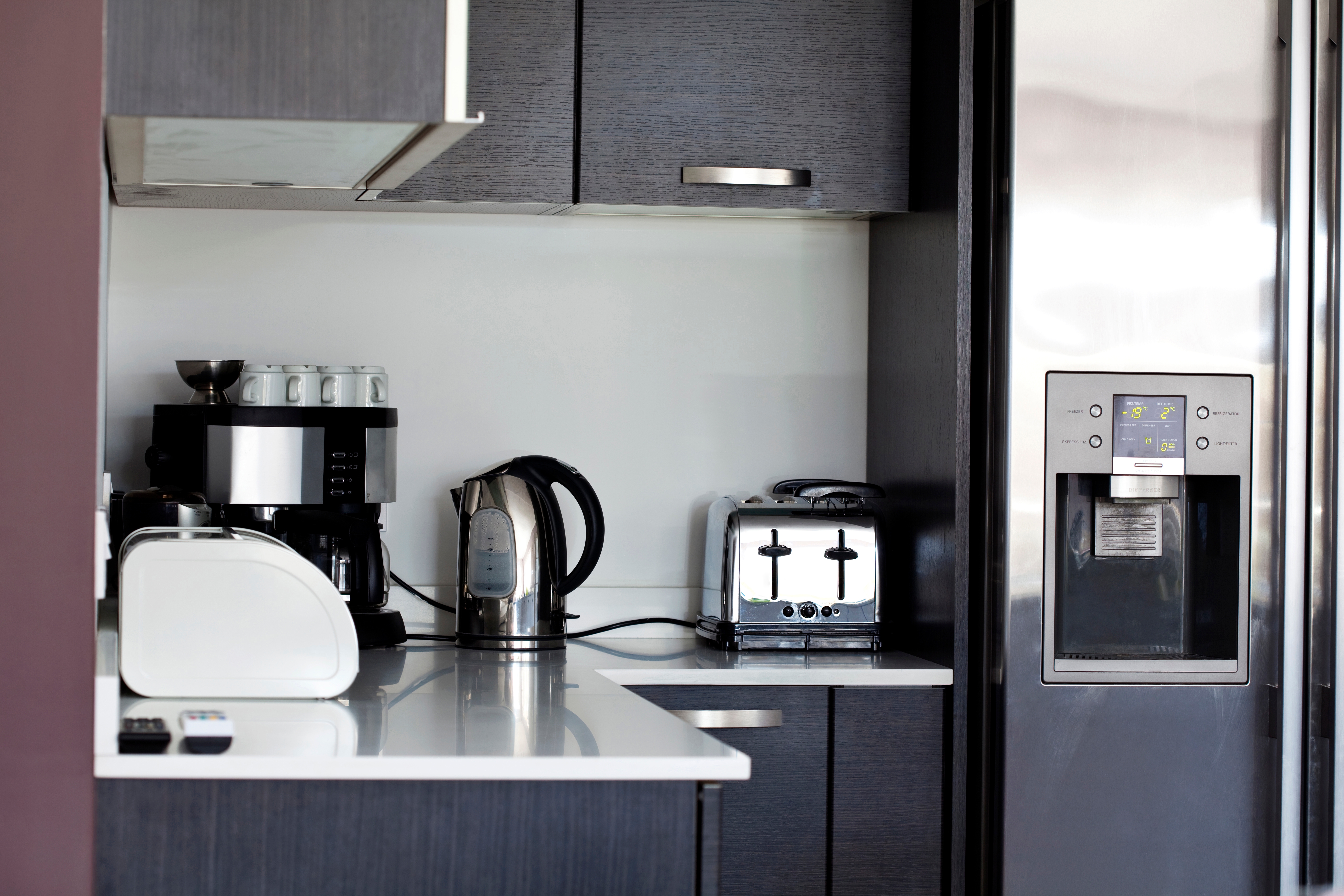 A modern kitchen counter with a coffee machine, a kettle, a toaster, and a refrigerator with an ice dispenser.