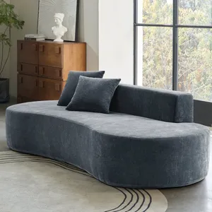 Curved dark gray sofa with two matching pillows set in a room with a large window, wooden dresser with a bust and book on top, geometric patterned rug, and a wooden side table with a lamp.