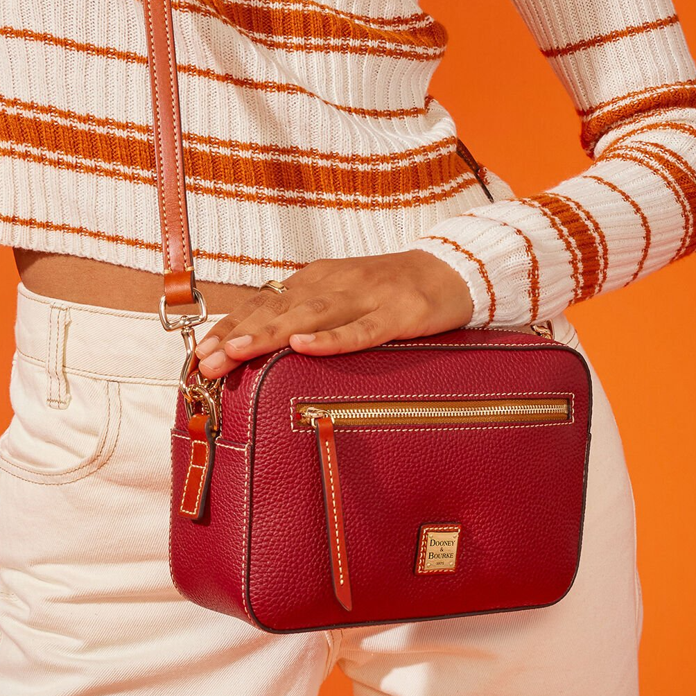 A person is holding a red crossbody bag with gold-tone hardware and a front zipper pocket.
