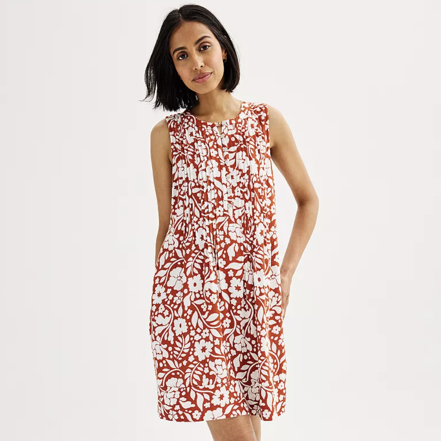 A woman is wearing a sleeveless, knee-length red and white floral dress.