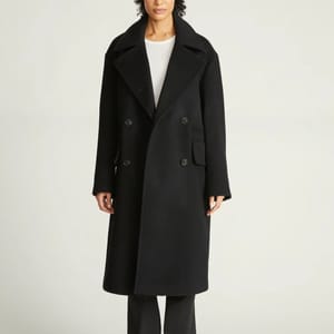 A woman modeling a long black overcoat with a white shirt and black pants.