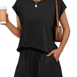 A woman wearing a black two-piece outfit consisting of a short-sleeve top and drawstring shorts, accessorized with a brown shoulder bag, a necklace, and holding a coffee cup.