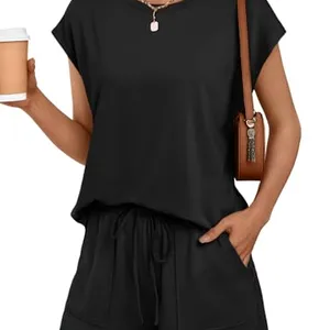 A woman wearing a black two-piece outfit consisting of a short-sleeve top and drawstring shorts, accessorized with a brown shoulder bag, a necklace, and holding a coffee cup.