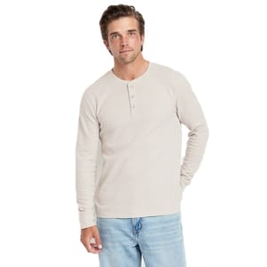 A man wears a light beige henley shirt paired with light blue jeans.