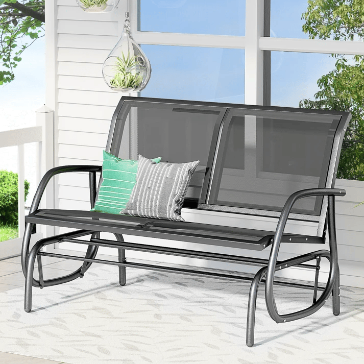 Outdoor glider bench with a metal frame and black cushions, accompanied by decorative pillows.