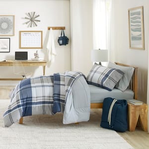 Plaid bedding set with comforter and pillows on a bed, a desk with a laptop, and wall decor in a bedroom.