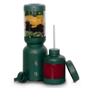 A dark green portable blender with fruit inside, accompanied by a matching detachable jar with a drinking straw and cap.