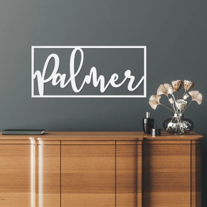 A wooden sideboard with a vase of flowers and cosmetics on top, and a personalized 'Palmer' wall decal above it.