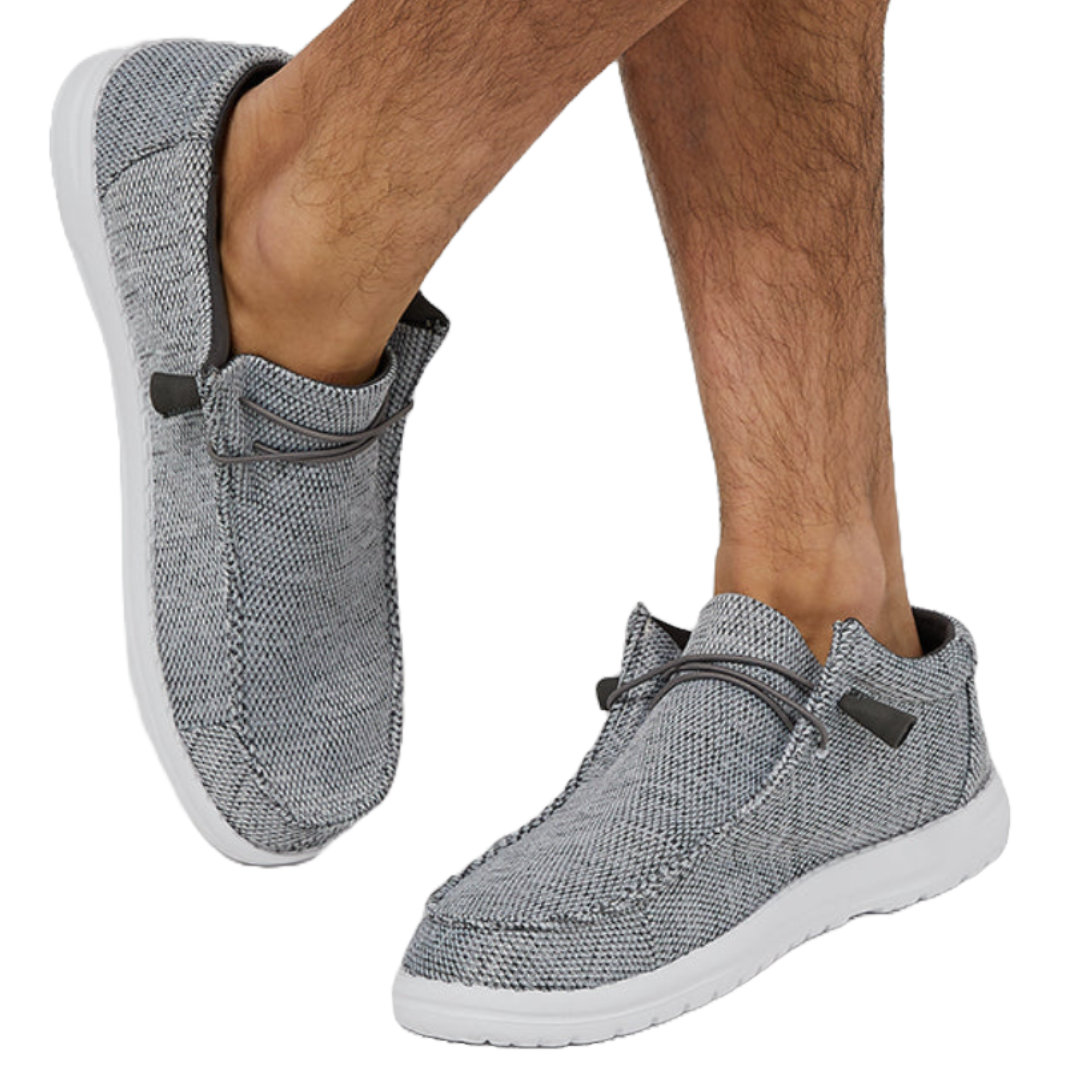 Gray casual slip-on shoes with white soles, featuring a textured fabric and decorative laces, worn by a person.