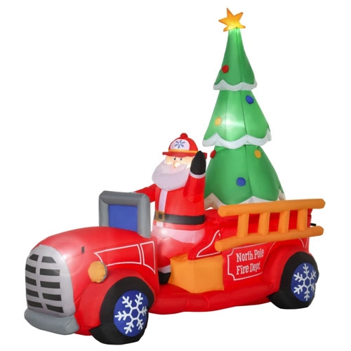 7.5ft inflatable Santa on a red fire truck with a large green Christmas tree in the back, marked \“North Pole Fire Dept\“ on the side. Santa is waving, and the wheels have snowflake designs.