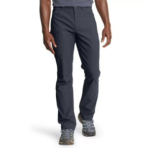 Men's dark-colored hiking pants with a straight fit, featuring a zippered side pocket and regular front pockets, paired with trail shoes.