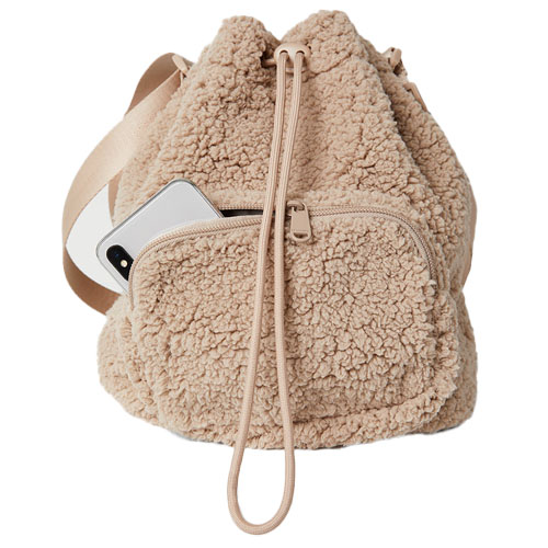 A beige sherpa drawstring backpack with a front zip pocket, featuring a phone partially visible in the pocket.