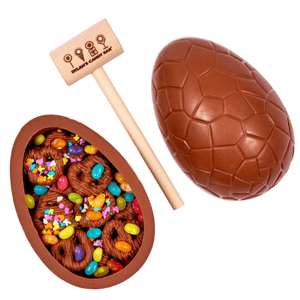 A breakable chocolate egg filled with colorful candies and chocolate-covered pretzels, accompanied by a small wooden mallet with the Dylan's Candy Bar logo.