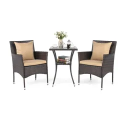 A patio set featuring two wicker chairs with beige cushions and a square table, adorned with tea cups, a teapot, books, and a vase of flowers.