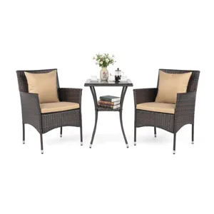 A patio set featuring two wicker chairs with beige cushions and a square table, adorned with tea cups, a teapot, books, and a vase of flowers.