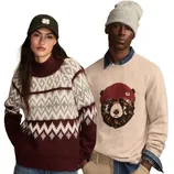Two people model clothing: one wears a maroon and white patterned sweater with a dark cap, and the other wears a beige sweater with a bear design paired with a gray beanie.