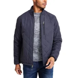 A man is wearing a dark quilted jacket with a zip-up design, over a gray sweater and blue jeans. The jacket features a chest zipper pocket and a high collar.