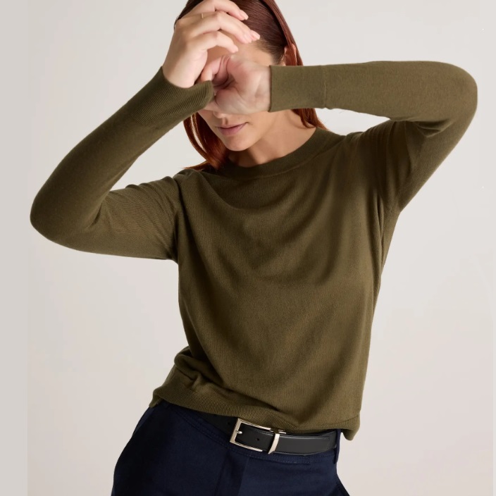 A woman wearing a green long-sleeved crew neck shirt paired with dark trousers and a black belt.