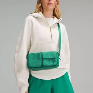 A woman wearing a white hoodie and green skirt with a green crossbody bag.