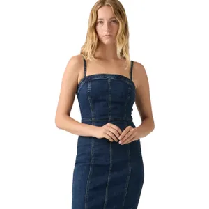 A woman wearing a dark blue denim dress with spaghetti straps and visible seam detailing.