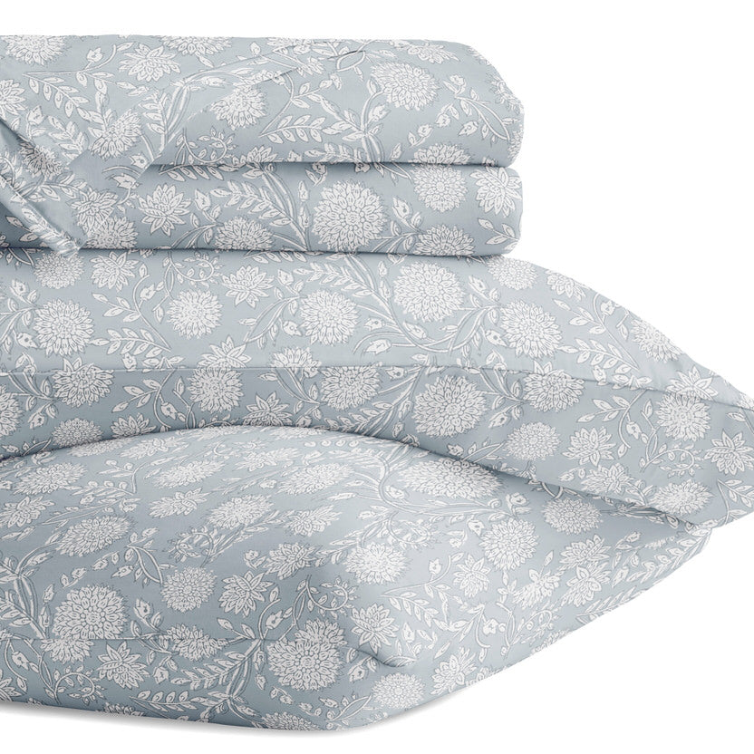 A stack of folded bedding, including a comforter and pillowcases, featuring a light blue and white floral pattern.