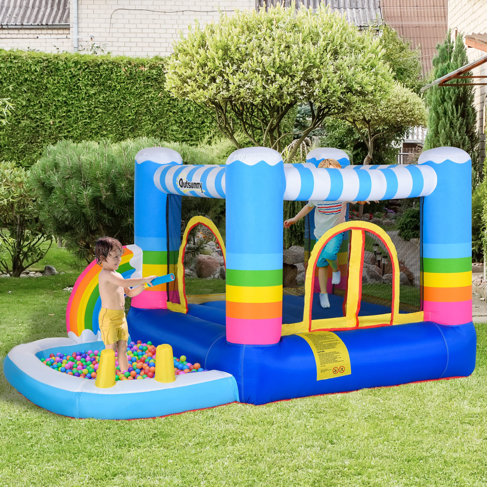 Inflatable bounce house with a rainbow theme, featuring a ball pit area, set up in a garden with children playing.