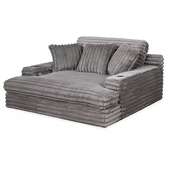 A plush, oversized gray chaise lounger with ribbed fabric, featuring wide arms with integrated cup holders and multiple coordinating pillows for added comfort.