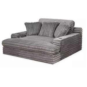A plush, oversized gray chaise lounger with ribbed fabric, featuring wide arms with integrated cup holders and multiple coordinating pillows for added comfort.