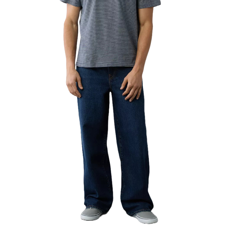 AE Baggy Jeans feature a loose fit with dark blue denim, a straight leg cut, and classic five-pocket styling. Paired with a striped short-sleeve shirt and grey slip-on shoes.