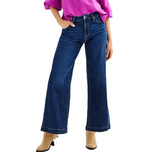 Woman wearing blue wide-leg jeans and a purple top, paired with beige shoes.