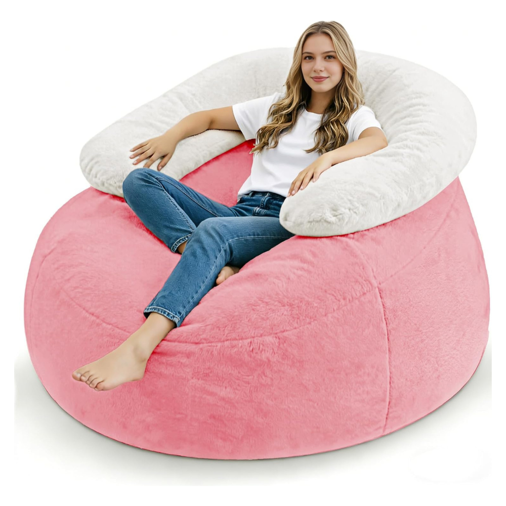 A woman is seated in a large, pink plush bean bag chair with a white, curved backrest. She's wearing a white t-shirt and blue jeans, relaxing comfortably.