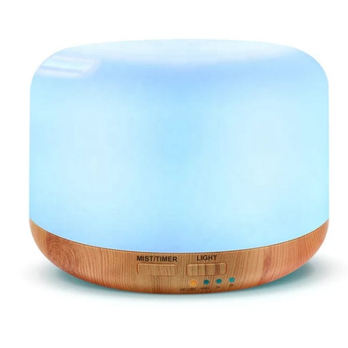 A round essential oil diffuser with a light wood base and glowing blue top, featuring controls for mist, timer, and light settings.