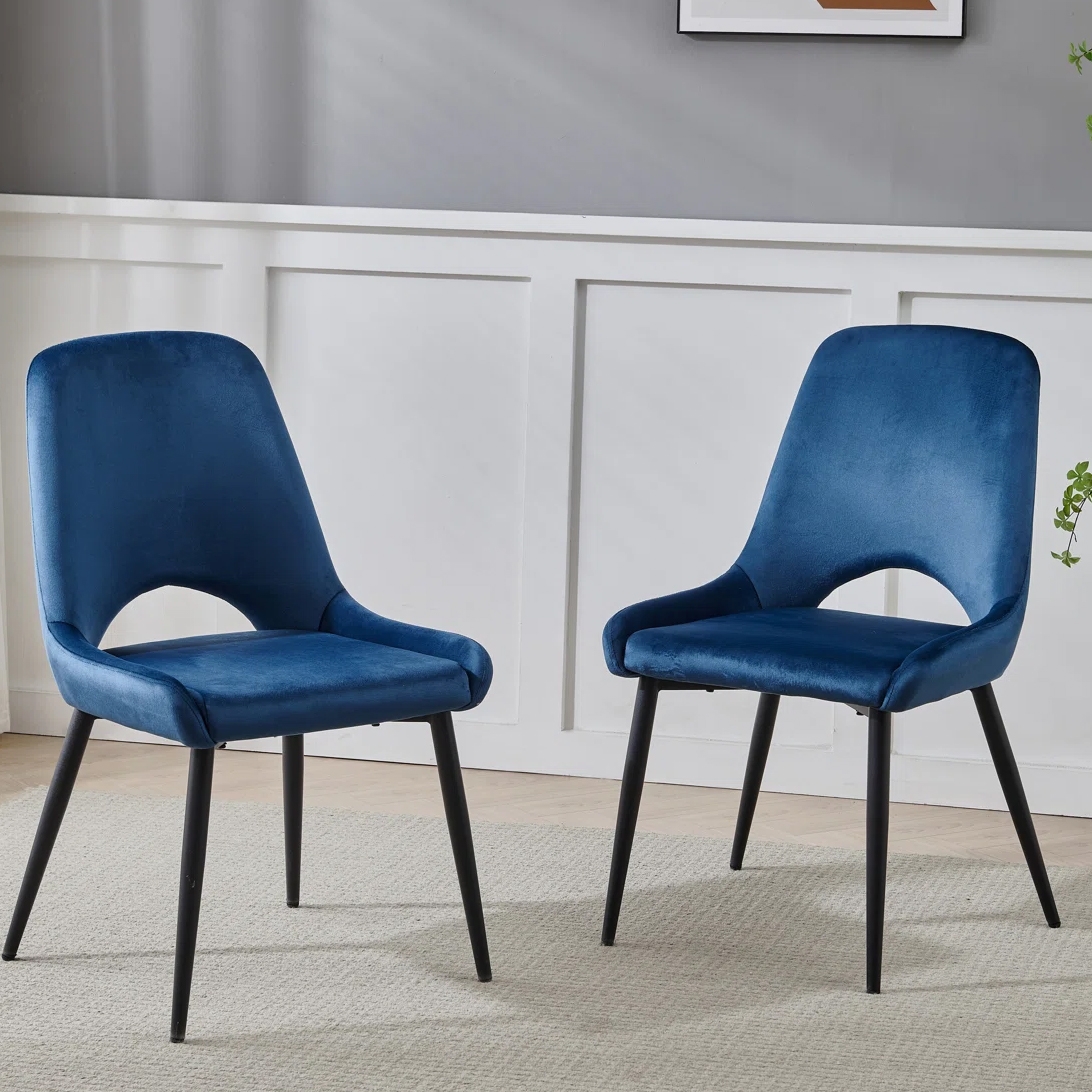 Two blue velvet upholstered chairs with black metal legs on a light rug, set against a gray wall with white paneling.