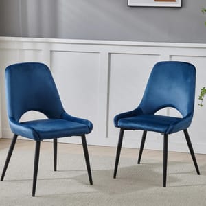 Two blue velvet upholstered chairs with black metal legs on a light rug, set against a gray wall with white paneling.