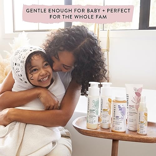 A smiling child is embraced by an adult, with five bottles of Honest Co. personal care products displayed in the foreground.