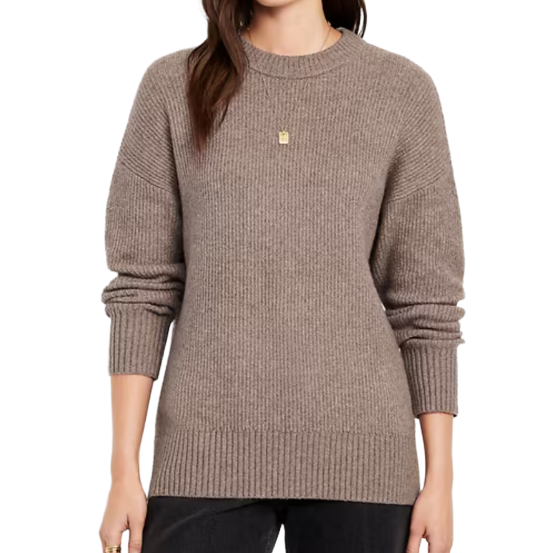 A woman wears a taupe ribbed-knit sweater with long sleeves and a crew neckline, paired with dark pants.