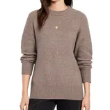 A woman wears a taupe ribbed-knit sweater with long sleeves and a crew neckline, paired with dark pants.