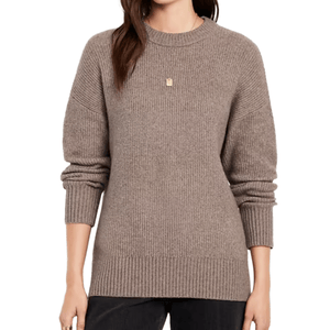 A woman wears a taupe ribbed-knit sweater with long sleeves and a crew neckline, paired with dark pants.