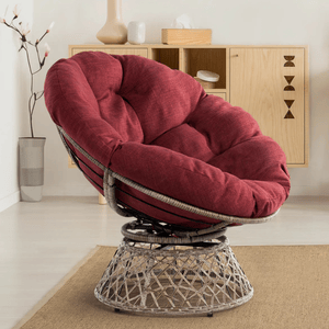 A comfortable chair with a deep red, cushioned seat and backrest. The frame is a wicker-style design with a swivel base, set in a minimalistic room with neutral decor.