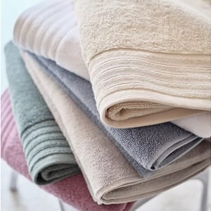 A stack of folded towels in various colors including beige, gray, green, and maroon.