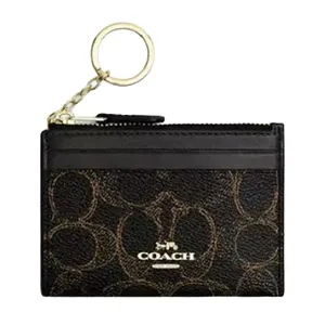 A Coach cardholder with a gold-toned keyring, featuring the brand's signature pattern and logo on a dark background.
