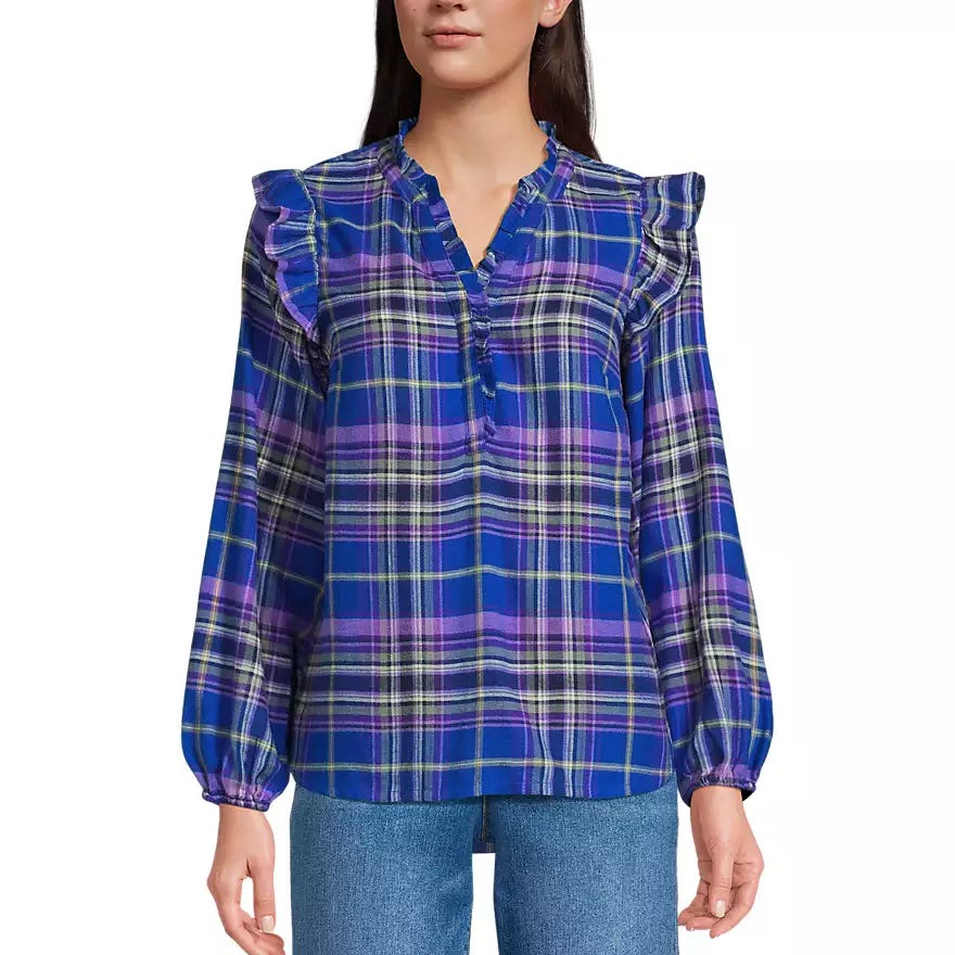 A woman is wearing a blue plaid blouse with ruffled shoulders and a V-neckline, paired with blue jeans.