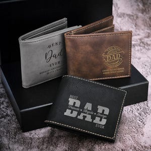 Three leather wallets with \“Best Dad Ever\“ inscriptions in different styles and colors—gray, brown, and black—featuring personalized family names on each.