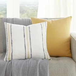 A beige sofa with a gray throw and two cushions, one with yellow stripes and the other solid yellow, is next to a small side table with a plant.